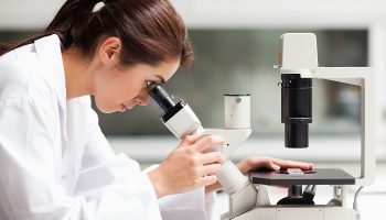 woman in lab coat using a microscope